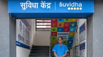 A woman in blue shirt standing and smiling with the Suvidha signboard above her head