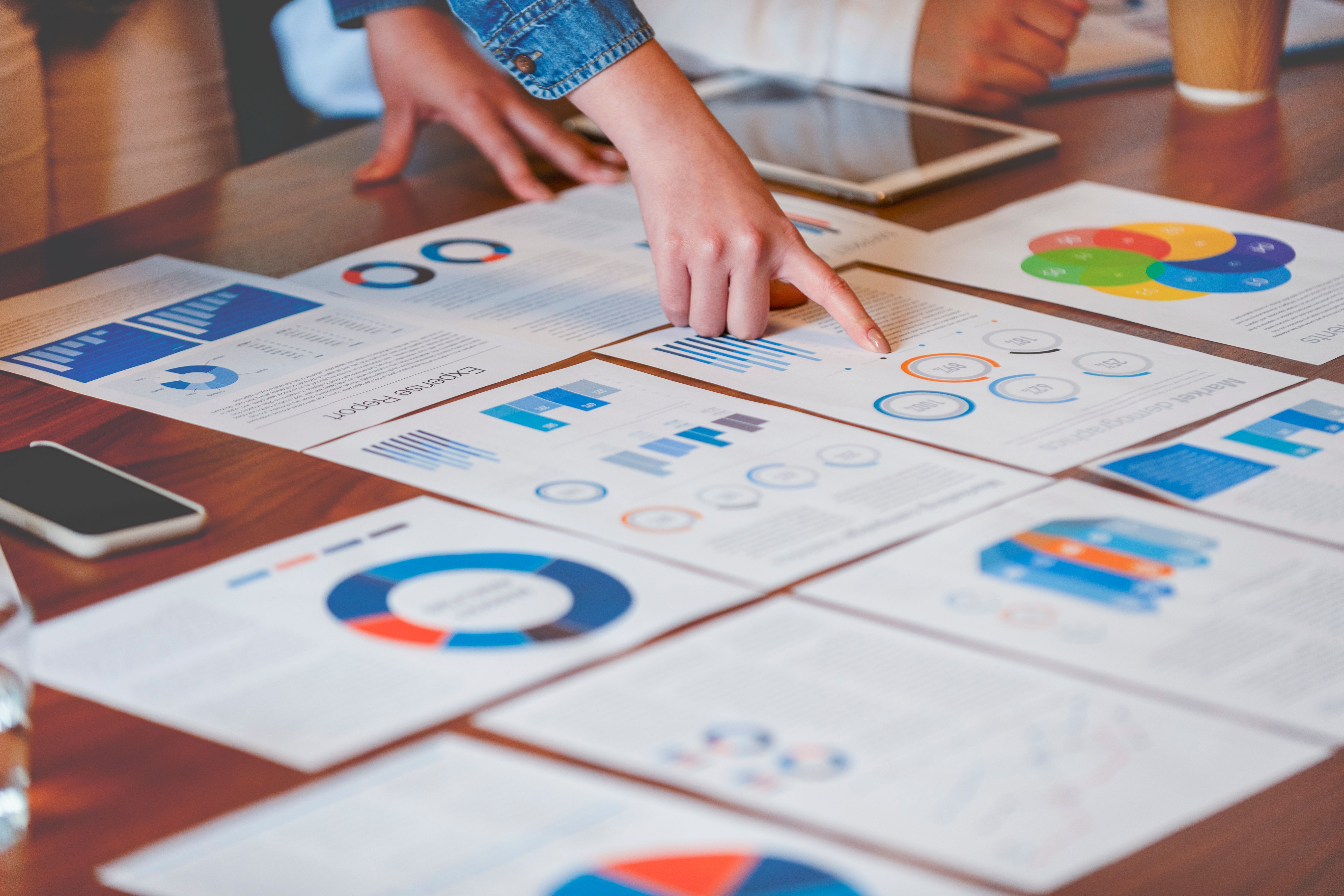 A hand points at business documents spread on a table, displaying colorful charts and graphs.