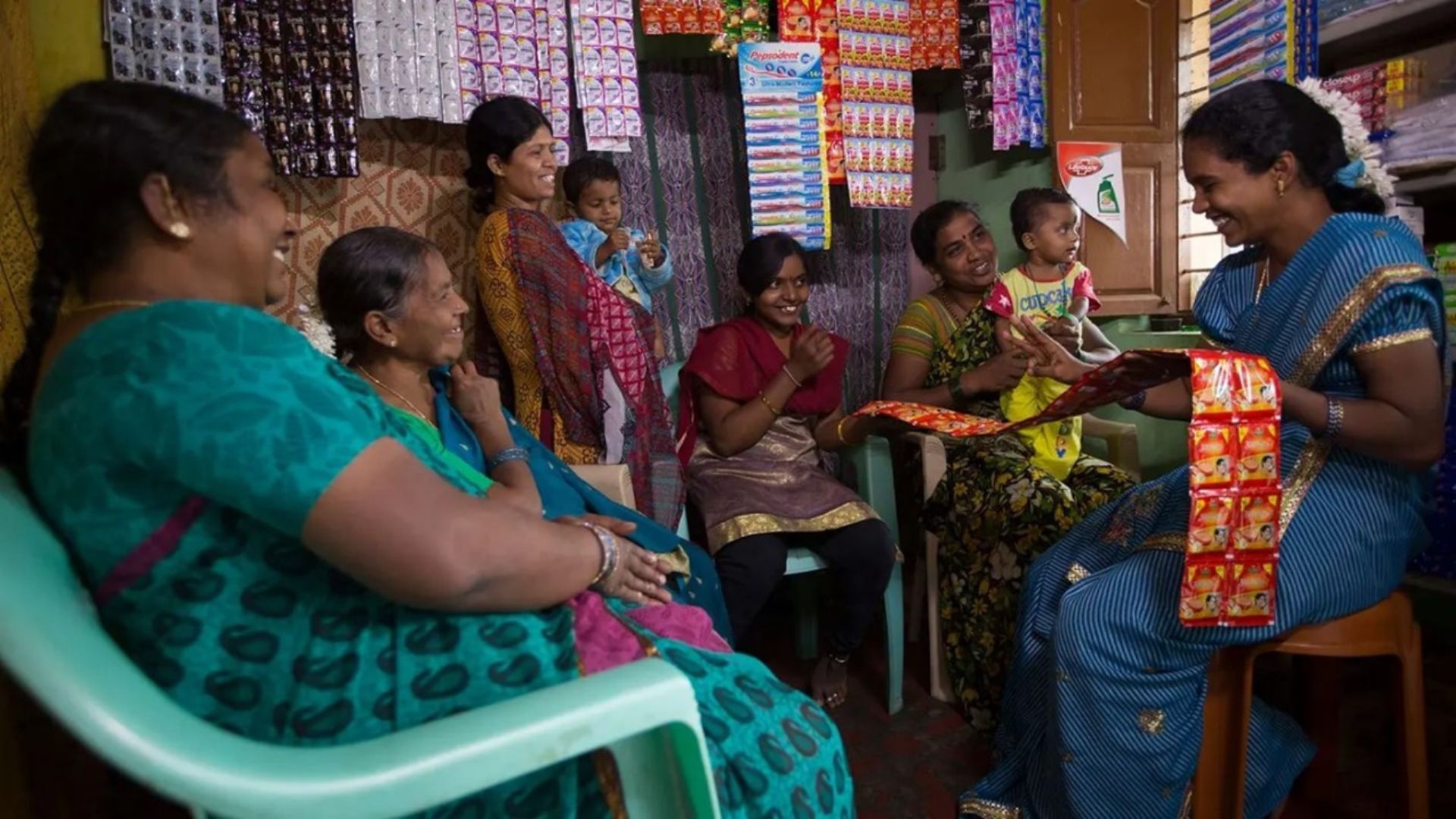A group of seated women smiling at each other surrounded by various products in a room