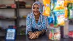 Smiling woman in floral attire at a small shop counter.