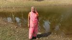 Woman in a pink sari stands beside a rural pond.