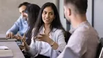 Three colleagues seated at a table in a modern office, engaged in an animated discussion during a meeting.