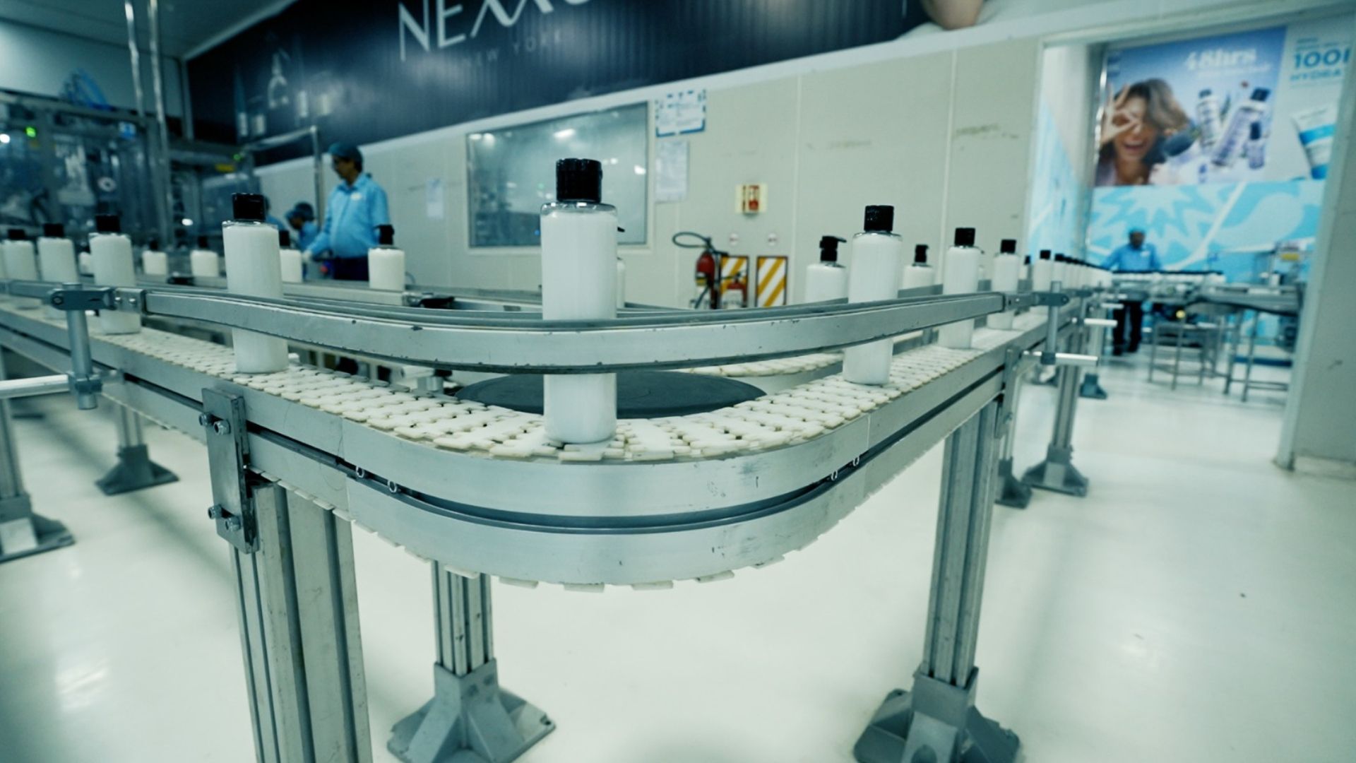 White plastic bottles move along an automated conveyor line in a clean manufacturing facility.