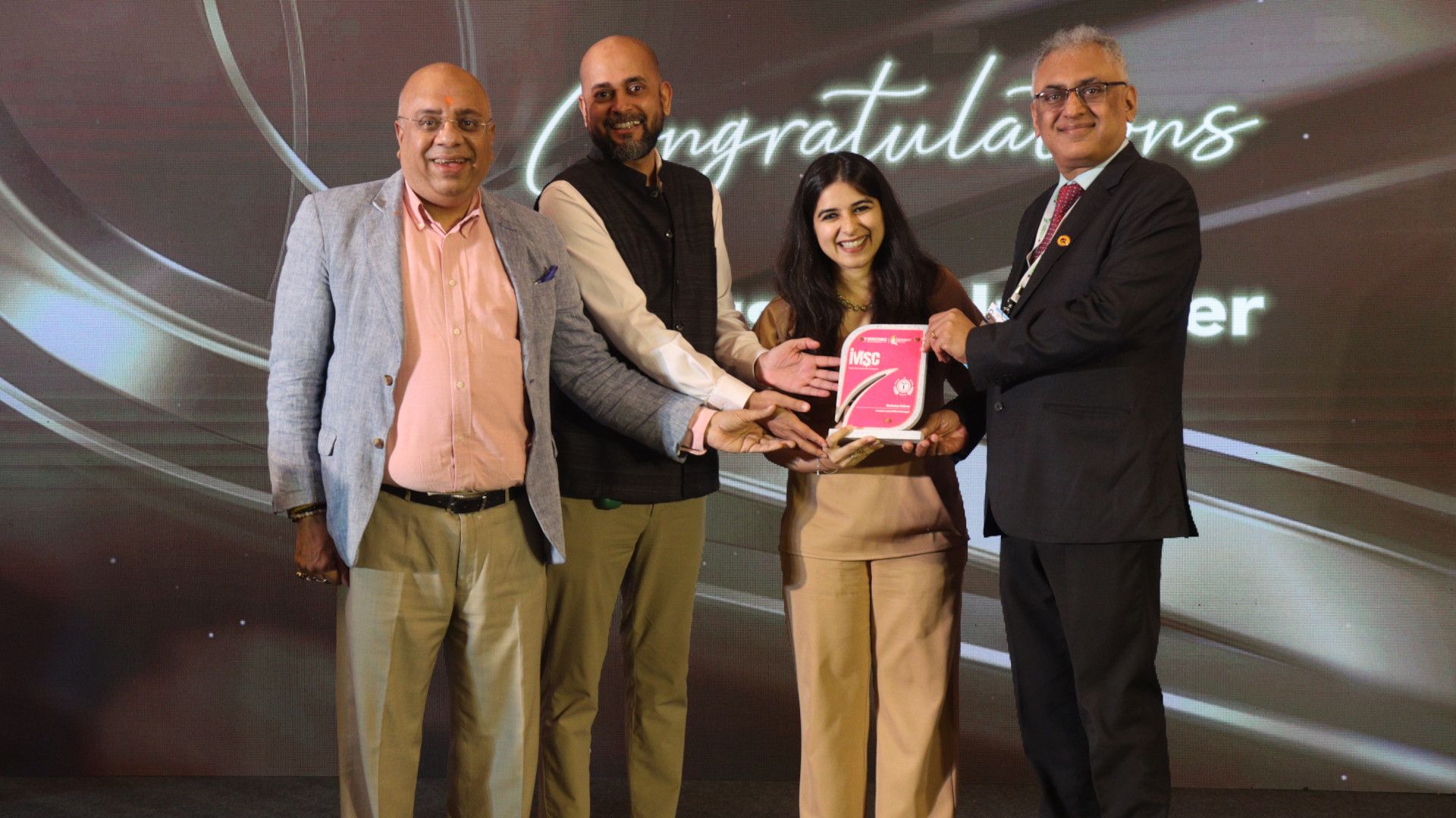 Four people stand together, smiling and holding an award plaque.