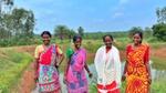 Four women in saris standing in the countryside.